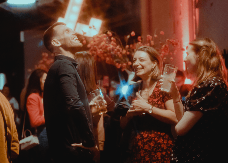 a photo of people laughing and chatting at a bar holding drinks